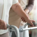 Old person with walking aid helped by nurse